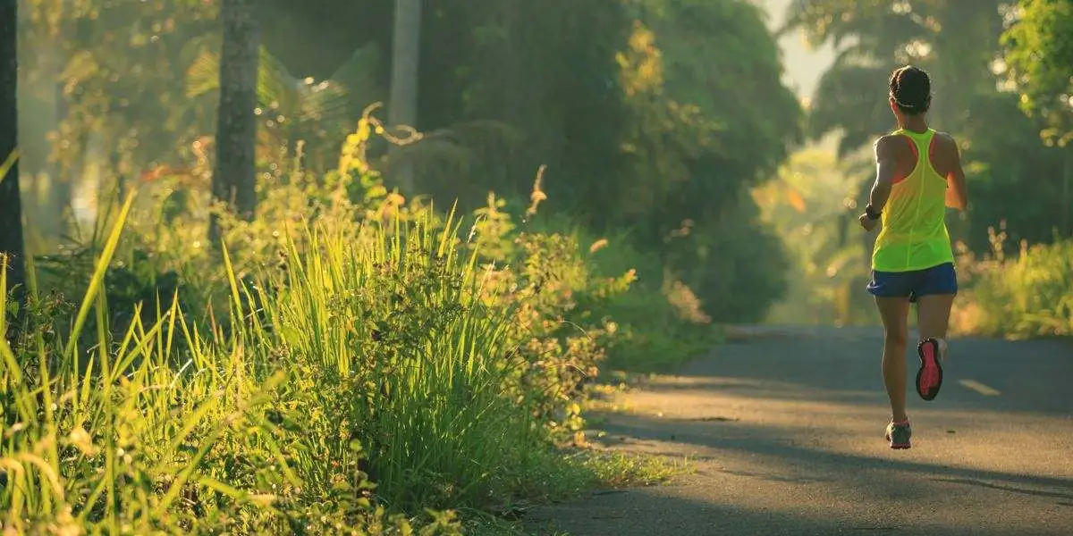 Mulher a correr de costas pelo asfalto ao lado de vegetação na estrada